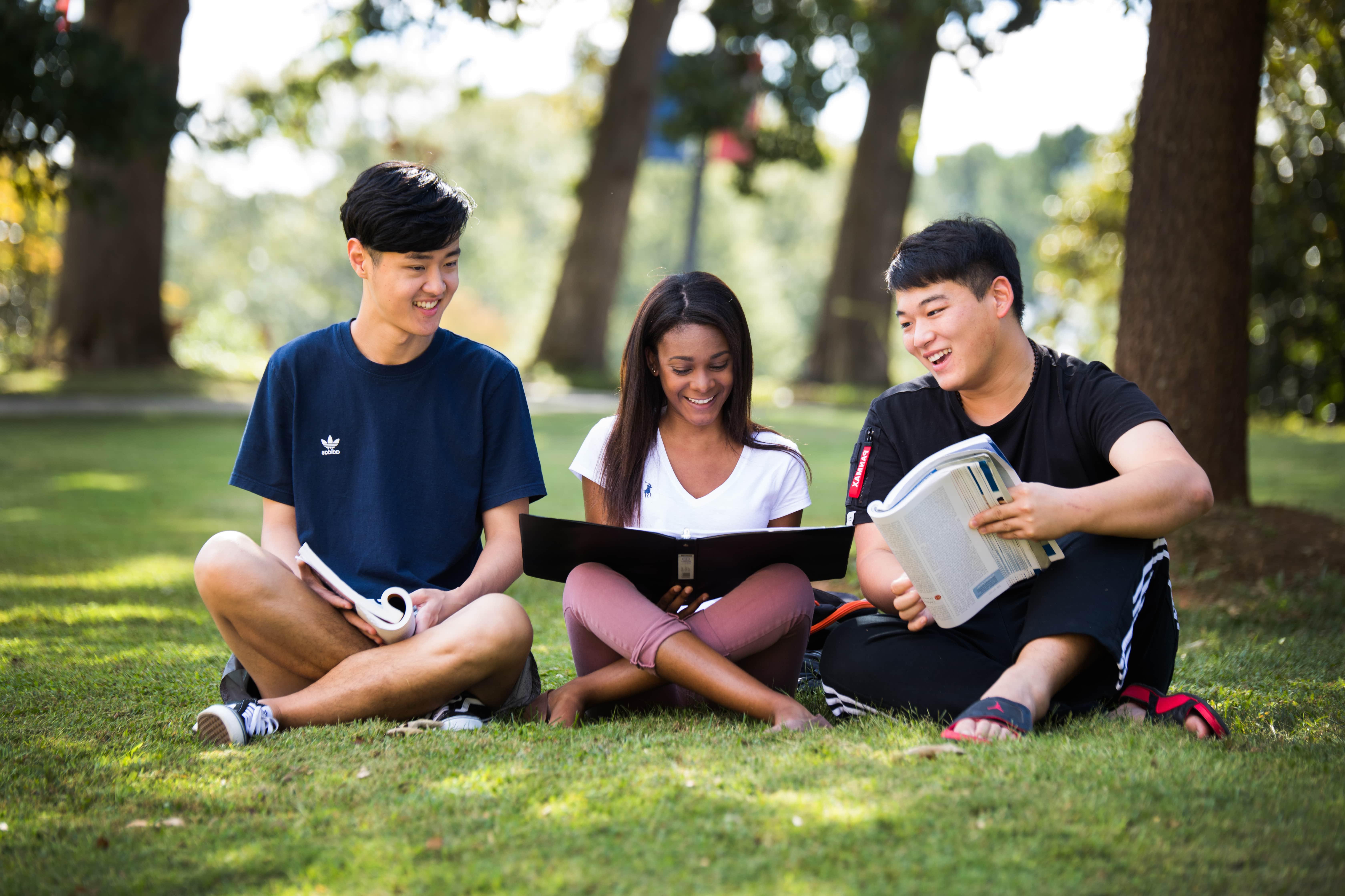 Three students sitting outside college of business reading together.