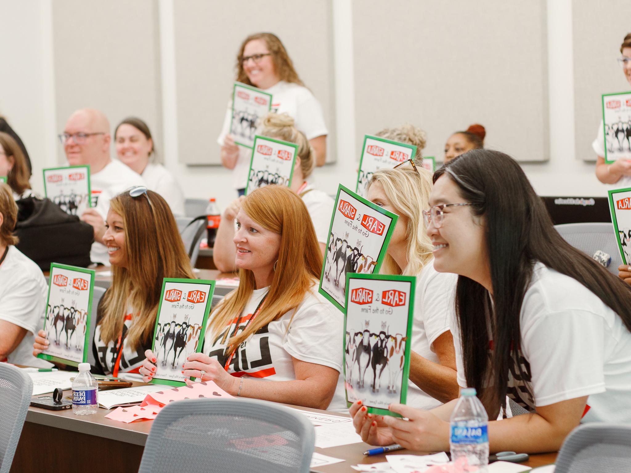 Students holding up flyers in a classroom as they learn to become teachers.